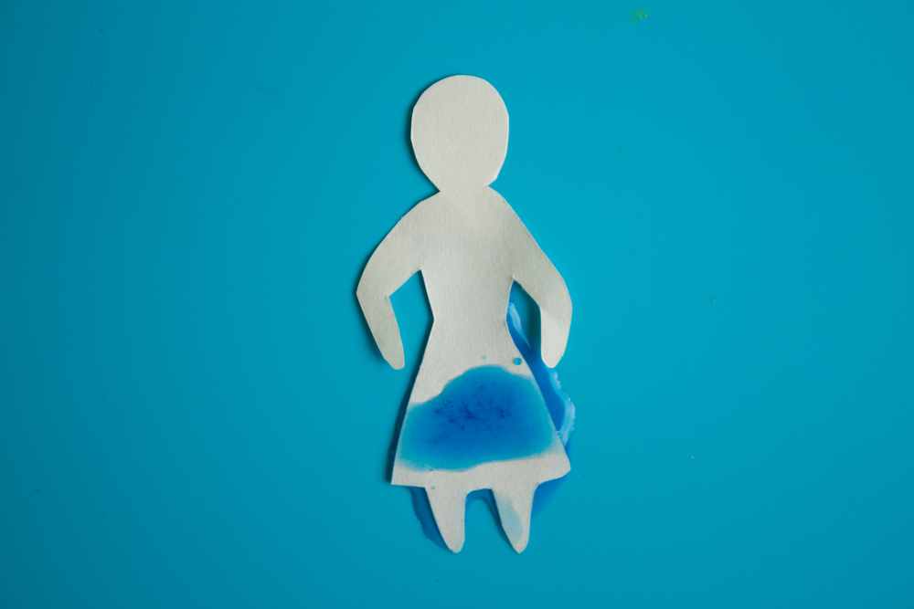 Paper cutout of woman on blue background, with blue liquid on skirt, symbolizing incontinence