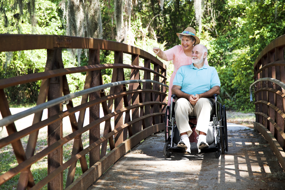 Senior woman pushing man across bridge in wheelchair