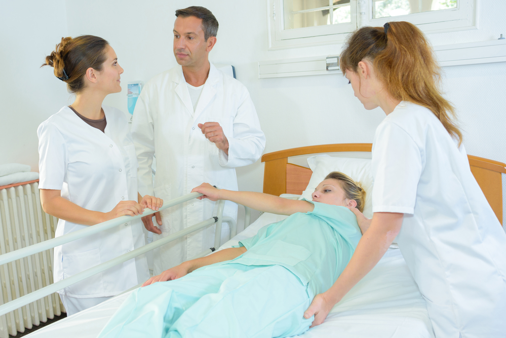 Nurse helping patient turn over in bed with 2 other hospital staff nearby