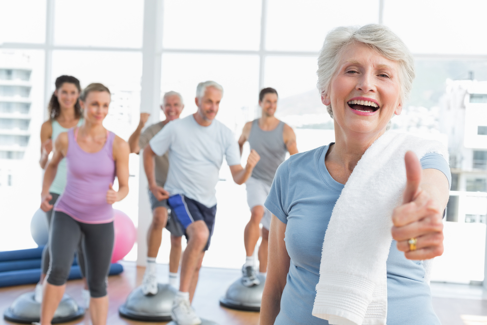 Senior woman giving thumbs up with seniors exercising in background
