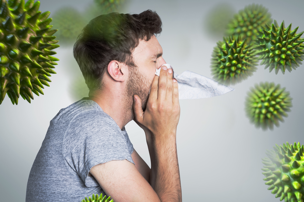 Man blowing nose, surrounded by large allergen particles